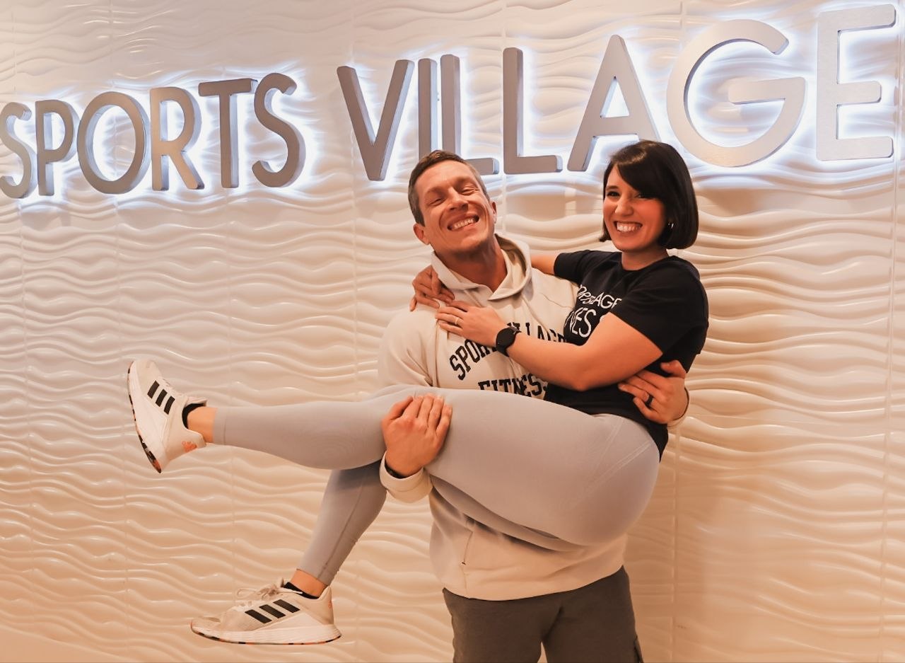 Andy lifting Holly beneath the Sports Village sign